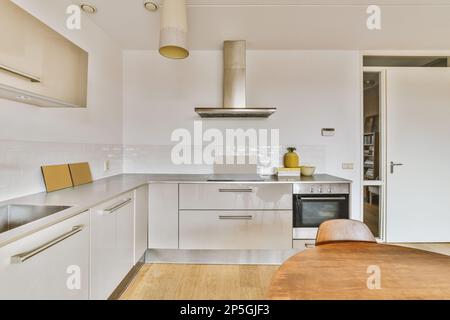 une cuisine avec parquet et armoires blanches au centre de l'image est une porte ouverte menant à une autre pièce Banque D'Images