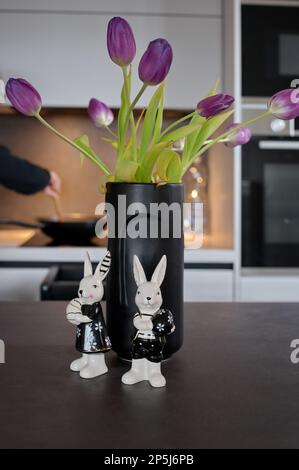 Lapins de Pâques en céramique devant un vase noir avec tulipes sur une table de cuisine Banque D'Images