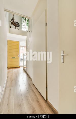 l'intérieur d'une maison avec parquet et murs blancs, une porte ouverte menant à une porte d'entrée jaune vif Banque D'Images