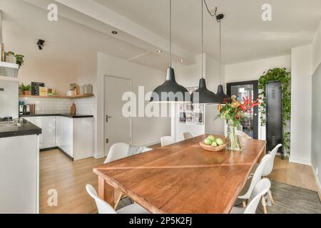 Amsterdam, pays-Bas - 10 avril 2021 : cuisine et salle à manger dans une maison avec table en bois, chaises blanches et suspensions noires suspendues au plafond Banque D'Images