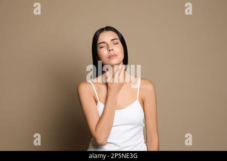 Jeune femme effectuant un auto-examen de la thyroïde sur fond beige Banque D'Images