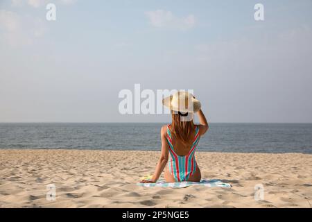 Femme avec une serviette de plage reposant sur une plage de sable, vue arrière. Espace pour le texte Banque D'Images