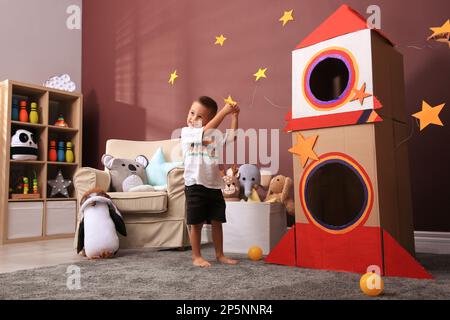 Mignon petit garçon jouant sur le sol près de la roquette en carton à la maison. Intérieur de la chambre des enfants Banque D'Images