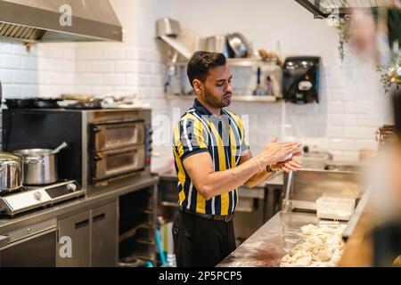 Jeune homme préparant des aliments frais dans une cuisine commerciale Banque D'Images