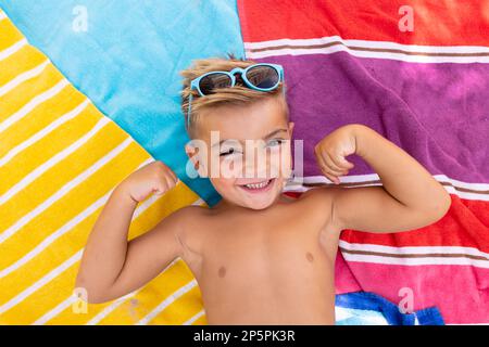 Portrait d'un garçon biracial heureux souriant et allongé sur une serviette au bord de la piscine Banque D'Images