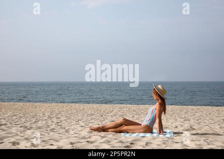 Femme avec serviette de plage reposant sur sable de mer, espace pour le texte Banque D'Images