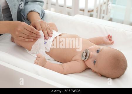 La mère change la couche de son bébé sur la table à la maison Banque D'Images