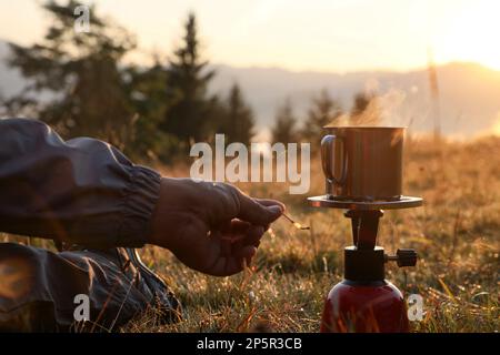 Homme faisant des boissons chaudes avec brûleur à gaz portable dans le camping de montagne, à proximité Banque D'Images