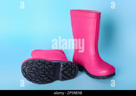 Paire de bottes en caoutchouc rose vif sur fond bleu clair Banque D'Images