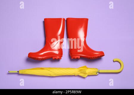 Paire de bottes en caoutchouc rouge avec parapluie jaune sur fond violet, plat Banque D'Images