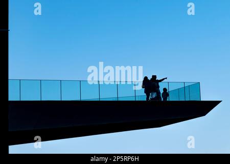 Une famille en silhouette sur une terrasse suspendue, tandis que le père indique un point éloigné avec son index Banque D'Images