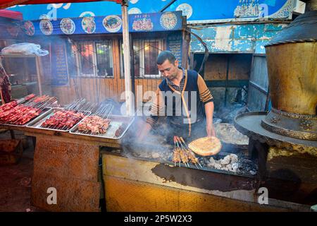 Vendeurs vendant de la viande cuite au barbecue et de la nourriture locale Uighour sur un marché traditionnel à Urumqi, Xinjiang, Chine Banque D'Images