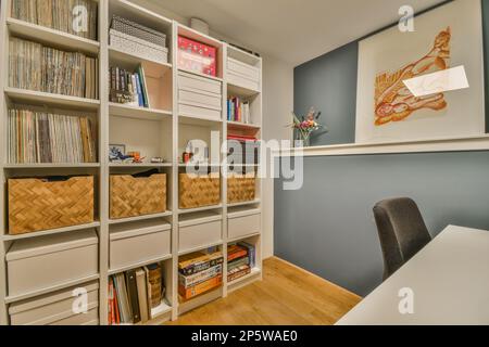 un bureau à la maison avec des étagères blanches sur le mur et des étagères remplies de livres, de magazines, de papiers et d'autres articles Banque D'Images