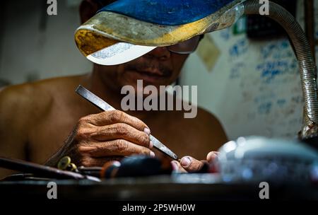 Un gros plan des mains et des pincettes d'un bijoutier et d'orfèvre travaillant sur un morceau d'or à l'intérieur du marché central de Phnom Penh, au Cambodge. Banque D'Images