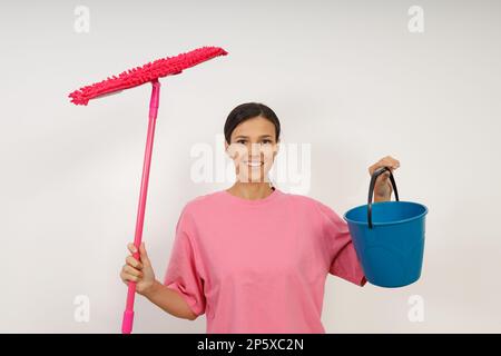 Bonne fille souriante faisant le nettoyage de la maison. Lavage des sols. Mignon jeune femme dans des vêtements décontractés et des gants en caoutchouc essuie le sol avec la vadrouille dans le salon r Banque D'Images