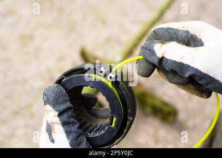 Un homme enfile une ligne pour couper l'herbe dans le tiroir d'une tondeuse à essence. Banque D'Images