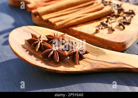 Étoiles anis épices étoiles sur une cuillère en bois, bâtons de cannelle et clous de girofle à l'arrière-plan. Ingrédients d'épices de pain d'épice. Banque D'Images