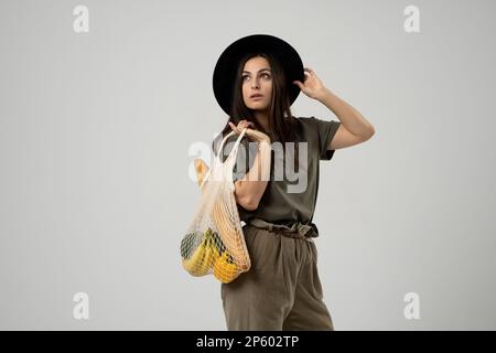 Une femme moderne et élégante avec un sac de shopping en filet avec des légumes sur le fond du studio.Le concept de nutrition saine, végétarisme Banque D'Images