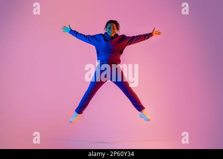 Sur toute la longueur du corps de jeune femme afro-américaine sportive sautant en forme d'étoile, s'amusant sur fond rose fluo Banque D'Images