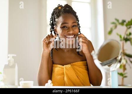 Un sourire parfait. Portrait d'une femme noire heureuse utilisant de la soie dentaire à la maison, faisant la routine du matin, assis à la table de vanité Banque D'Images