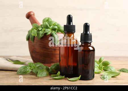 Bouteilles d'huile essentielle de basilic près du mortier avec feuilles et pilon sur une table en bois Banque D'Images