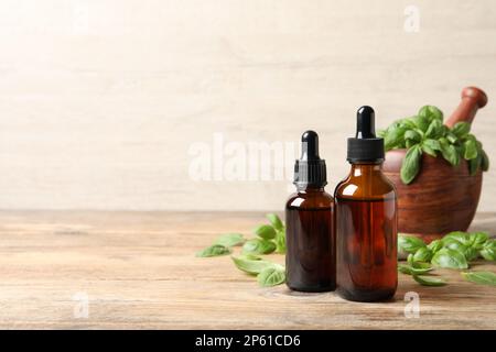 Bouteilles d'huile essentielle de basilic près du mortier avec feuilles et pilon sur une table en bois. Espace pour le texte Banque D'Images