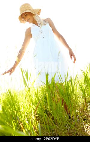 Aucune lame d'herbe n'est la même... Une jeune femme insouciante touchant l'herbe longue lorsqu'elle se balade dans un pré. Banque D'Images