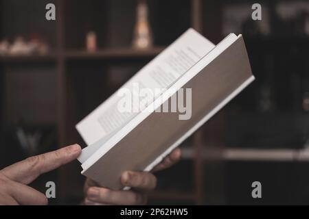 les mains des hommes tiennent un livre ouvert dans une couverture blanche sur un fond sombre. Banque D'Images