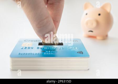 Banque de porc avec fond blanc de carte de crédit. Mettez une pièce dans la tirelire. Le concept de stockage de l'argent sur carte. la main met une pièce de monnaie dans la piggy ba Banque D'Images
