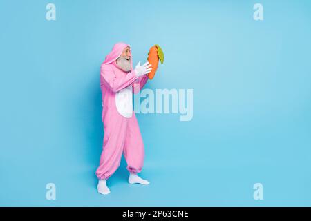 Photo pleine longueur de penseur funky impressionné gars habillé bunny kigurumi capture carotte vide espace isolé couleur bleu arrière-plan Banque D'Images