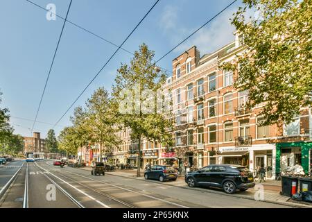 Amsterdam, pays-Bas - 10 avril 2021 : rue de la ville avec des voitures garées sur le côté et des bâtiments à l'arrière-plan, des arbres bordant les trottoirs Banque D'Images