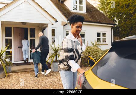 Une femme charge la voiture électrique sur l'allée à l'extérieur de la maison Banque D'Images