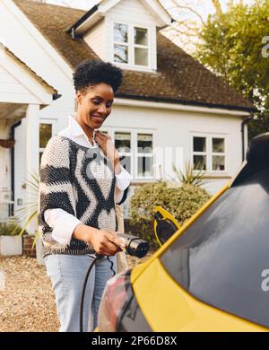 Une femme charge la voiture électrique sur l'allée à l'extérieur de la maison Banque D'Images