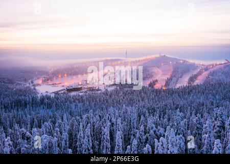 Brume au coucher du soleil sur la station de ski de Ruka et bois neigeux en hiver, vue aérienne, Kuusamo, Ostrobothnia du Nord, Laponie, Finlande, Europe Banque D'Images