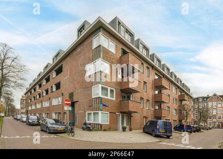un immeuble d'appartements avec des voitures garées dans la rue en face de lui et ciel bleu au-dessus du ciel Banque D'Images