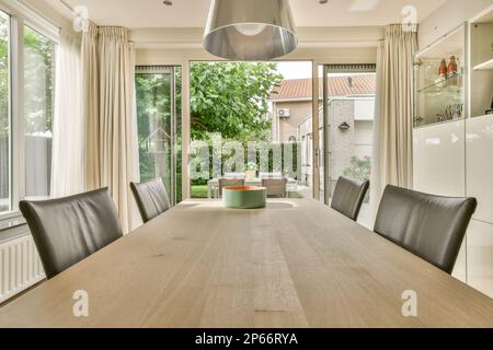 Amsterdam, pays-Bas - 10 avril 2021 : une table et des chaises dans une salle à manger avec portes vitrées coulissantes menant à un patio extérieur, entouré d'arbres Banque D'Images