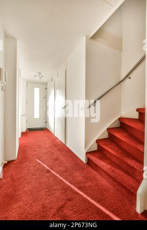 une moquette rouge dans une pièce blanche avec des escaliers menant au deuxième étage et une porte ouverte sur le côté droit Banque D'Images