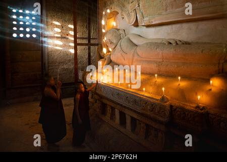 Deux moines débutants éclairant la bougie par la statue bouddhiste à l'intérieur du temple, Bagan (Pagan), site du patrimoine mondial de l'UNESCO, Myanmar (Birmanie), Asie Banque D'Images