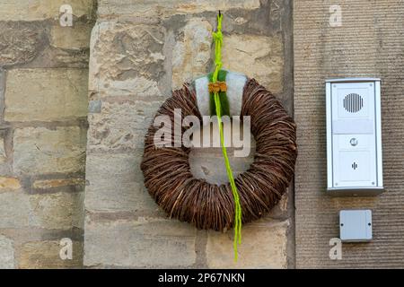 Une couronne tissée à partir de branches sèches est suspendue sur un mur en pierre. Interphone installé à proximité. Banque D'Images