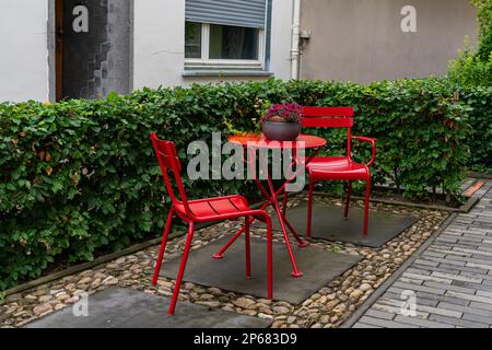 Deux chaises en métal et une table peinte de peinture rouge dans la cour de la maison. Entouré de végétation verte. Banque D'Images