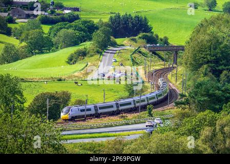 Un train inclinable Avantini Pendolino vu sur les courbes de la ligne principale de la côte ouest à Beck foot près de Tebay, avec la M6 longeant. Banque D'Images