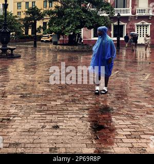 Un homme afro-colombien, portant un imperméable, marche sur une place pavée au milieu de la pluie pendant la saison des pluies annuelle à Cartagena, Colombie. Banque D'Images