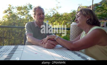 Un couple senior tenant les mains assis dans la cour intérieure du patio. Moment romantique authentique entre deux époux et une femme plus âgés. Concept d'amour mûr Banque D'Images