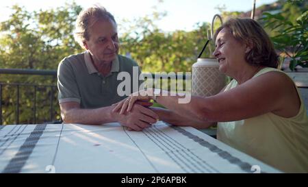 Un couple senior tenant les mains assis dans la cour intérieure du patio. Moment romantique authentique entre deux époux et une femme plus âgés. Concept d'amour mûr Banque D'Images