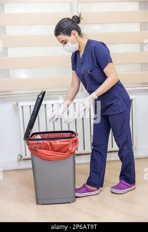 L'infirmière jette les déchets médicaux dans la poubelle de déchets médicaux du bureau. Une infirmière porte un sac poubelle rouge. Femme de ménage et corbeille des infections à l'hôpital. Infecti Banque D'Images