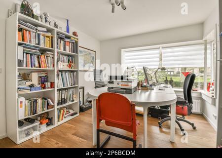 un bureau à la maison avec beaucoup de livres sur les étagères et une chaise rouge devant les bibliothèques Banque D'Images