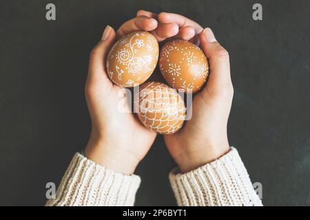 Mains tenant des oeufs de pâques peints à la main sur fond noir rustique métallique, vue de dessus Banque D'Images