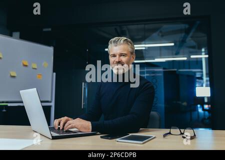 Portrait d'un homme d'affaires adulte âgé à l'intérieur du bureau, d'un investisseur masculin gris aux cheveux souriants sur le lieu de travail et regardant l'appareil photo. Banque D'Images