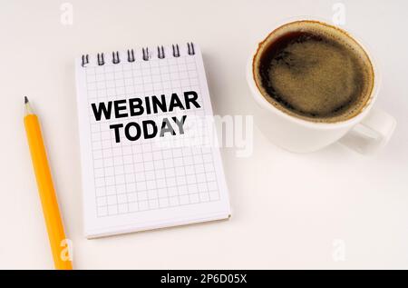 Concept d'entreprise. Sur une surface blanche, une tasse de café, un crayon et un bloc-notes avec l'inscription - webinaire aujourd'hui Banque D'Images