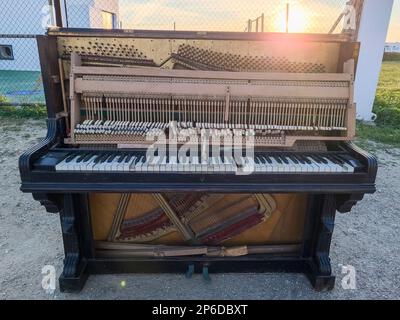 Vieux piano abandonné dans la rue avec un coucher de soleil en arrière-plan Banque D'Images